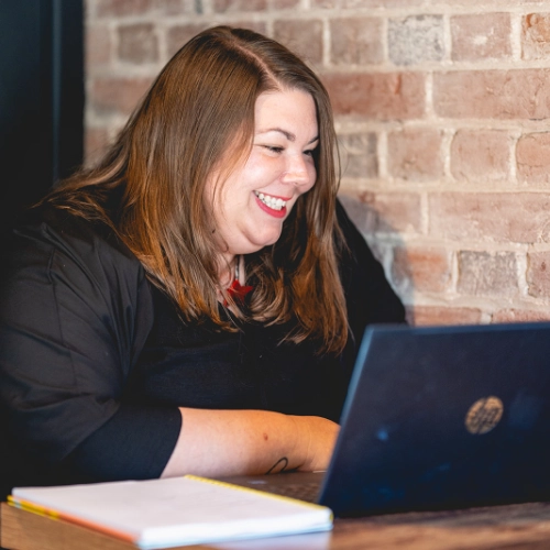 Hayley Shelley smiling while sitting at a desk, working on a laptop.